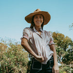 Woman wearing a straw hat and a patterned shirt standing outdoors with trees in the background
