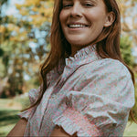 Woman smiling outdoors with trees and blue sky in the background