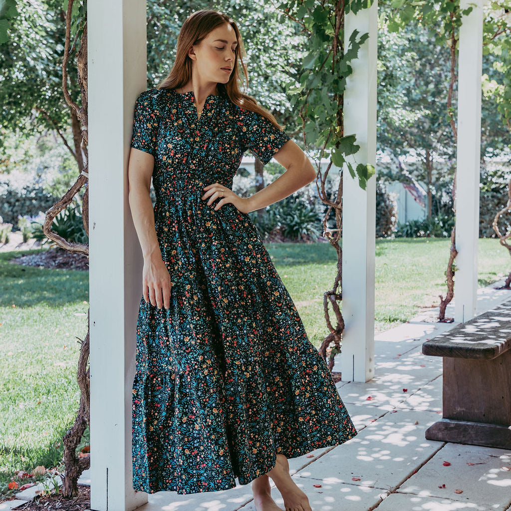 Woman in a floral dress standing under a pergola with greenery