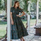 Woman in a floral dress standing under a pergola with greenery