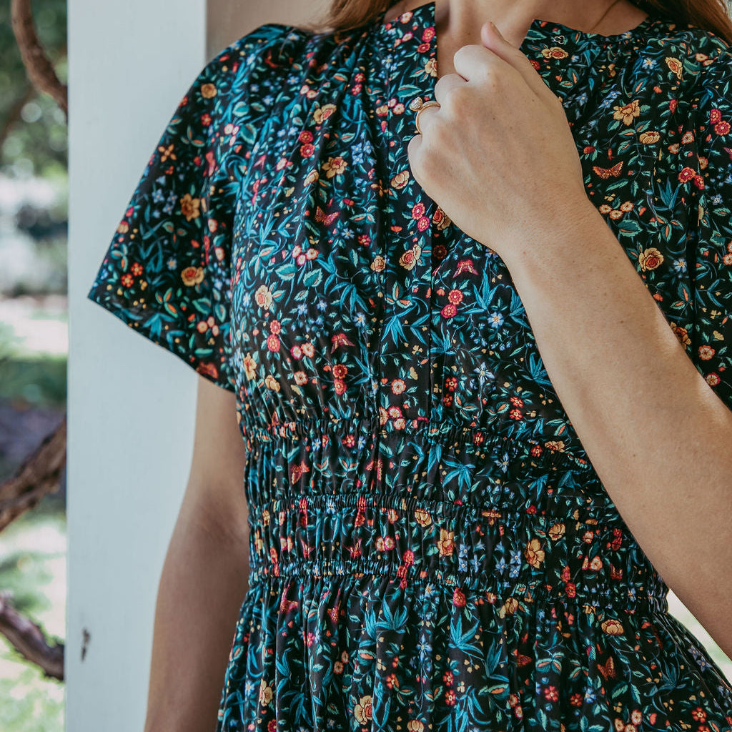 Woman wearing a dark floral dress with a blurred outdoor background