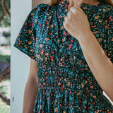 Woman wearing a dark floral dress with a blurred outdoor background