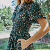 Woman wearing a floral dress standing outdoors with greenery in the background