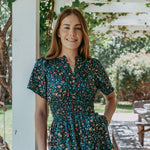 Woman wearing a floral dress standing outdoors under a white pergola.