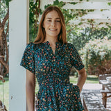 Woman wearing a floral dress standing outdoors under a white pergola.