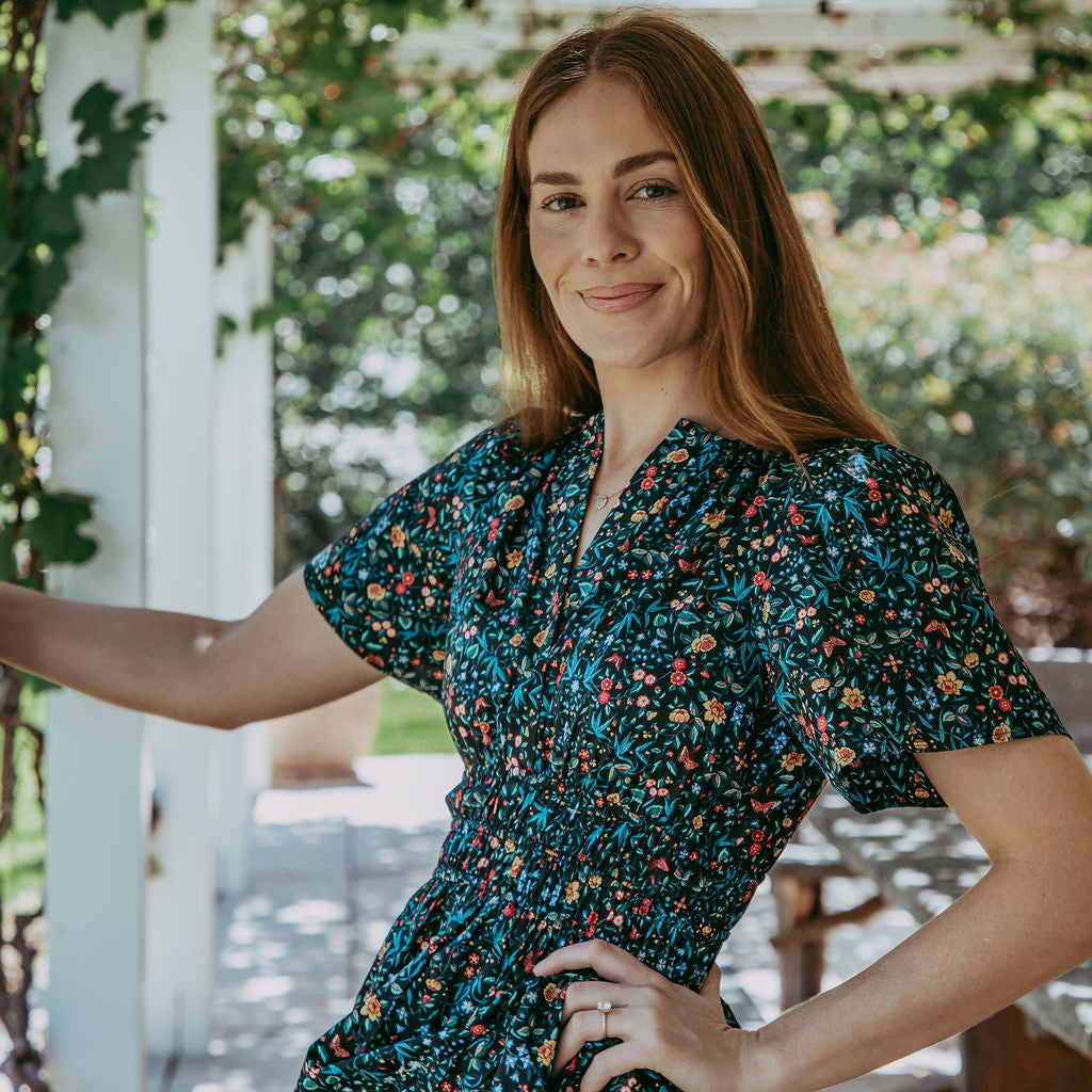 Woman in a floral dress standing outdoors with greenery in the background
