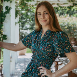 Woman in a floral dress standing outdoors with greenery in the background