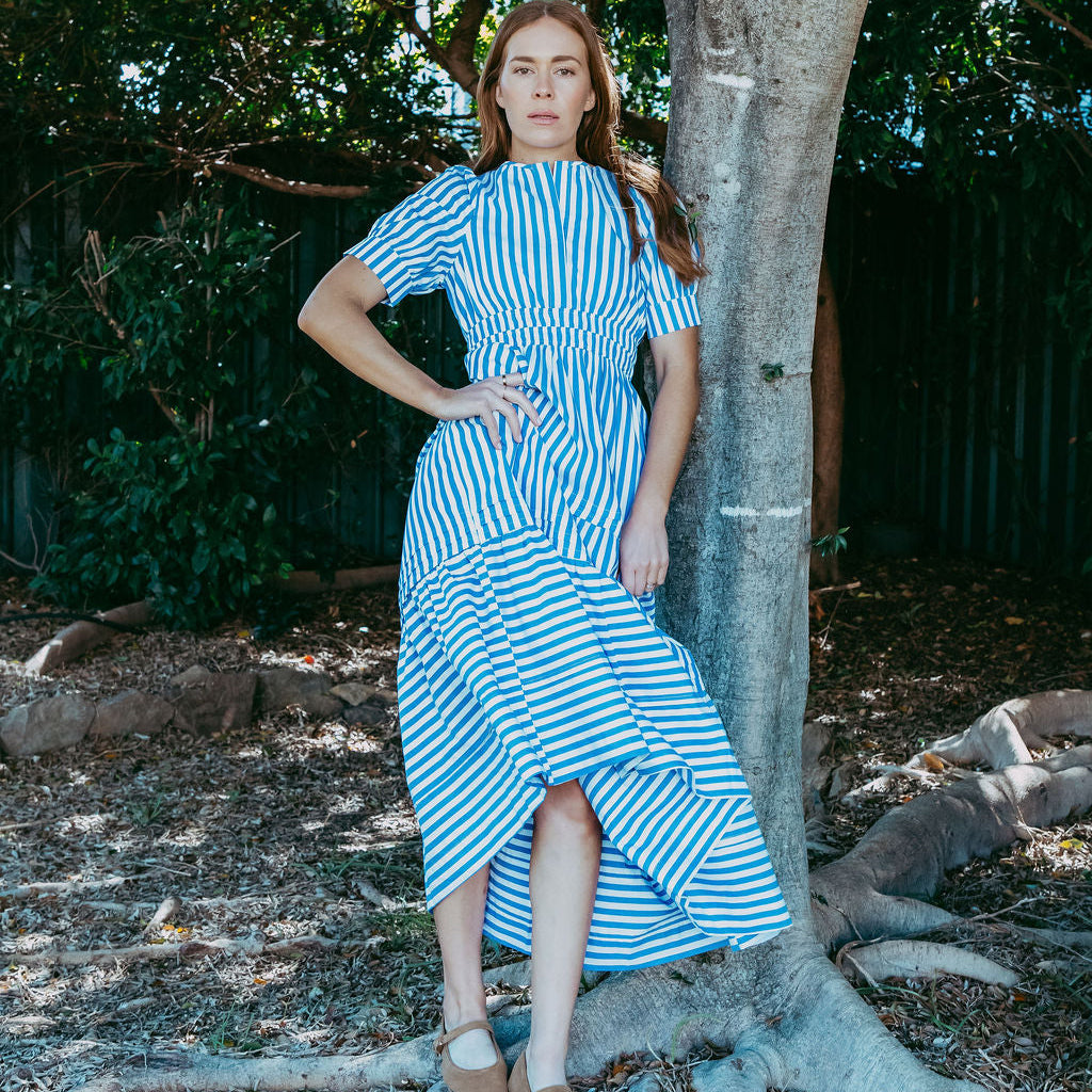Woman in a blue striped dress standing next to a tree in a natural setting