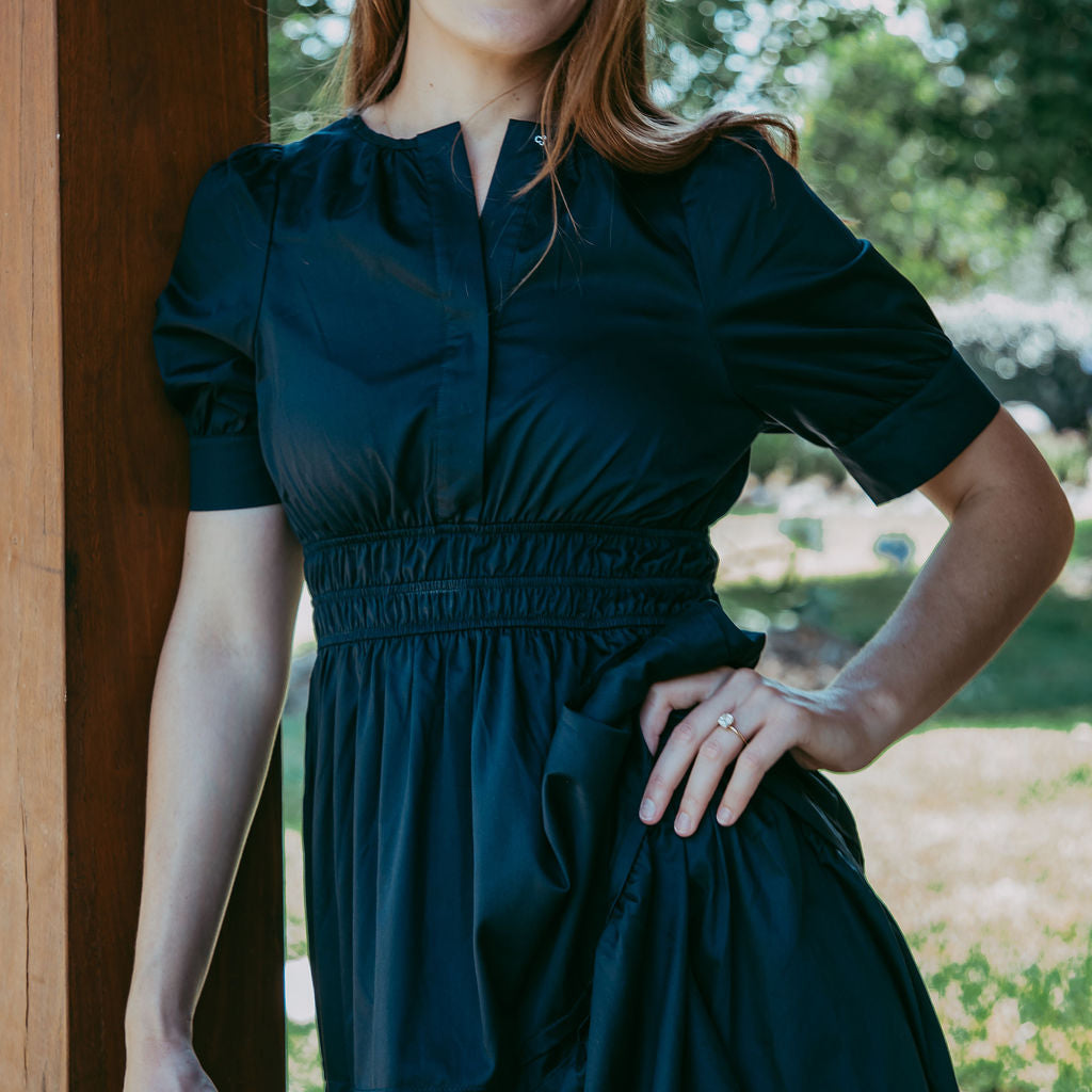Woman wearing a dark green dress standing outdoors with trees in the background