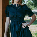 Woman wearing a dark green dress standing outdoors with trees in the background
