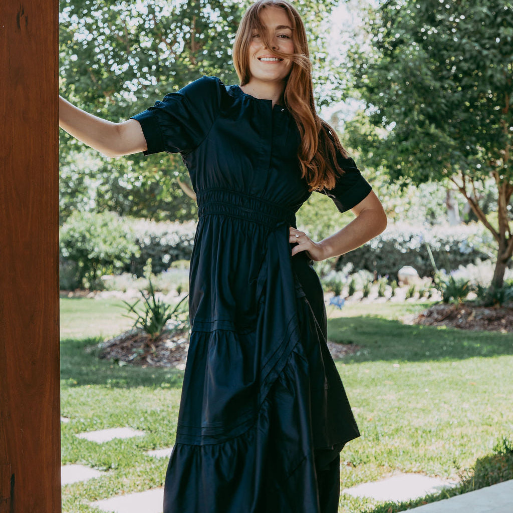 Woman in a dark green dress standing outdoors with trees and grass in the background