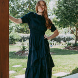 Woman in a dark green dress standing outdoors with trees and grass in the background