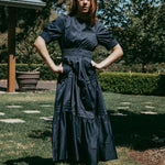 Woman in a dark blue dress standing outdoors on grass with trees in the background