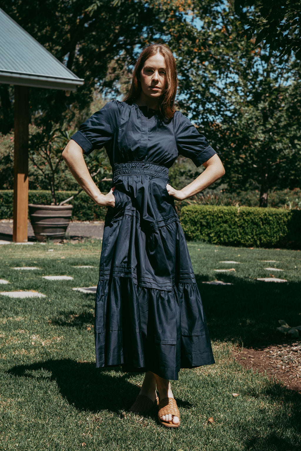 Woman in a dark blue dress standing outdoors on grass with trees in the background