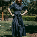 Woman in a dark blue dress standing outdoors on grass with trees in the background