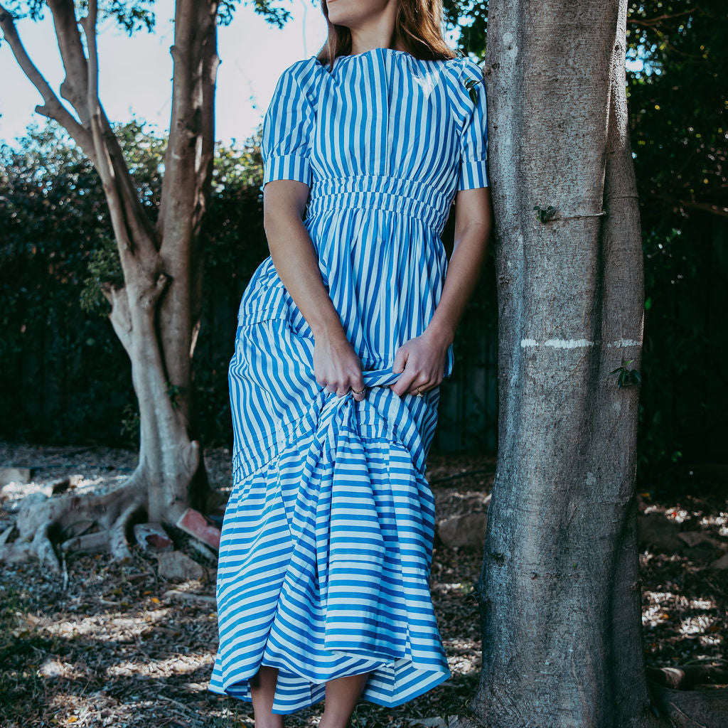 Woman in a blue and white striped dress standing next to a tree in a natural setting