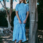 Woman in a blue and white striped dress standing next to a tree in a natural setting
