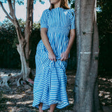 Woman in a blue and white striped dress standing next to a tree in a natural setting