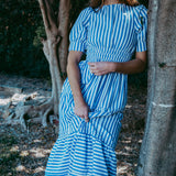Woman in a blue and white striped dress standing next to a tree in a natural setting