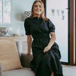 Woman in a black dress sitting on a wicker chair indoors.
