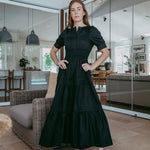 Woman in a black dress standing in a modern indoor setting with glass walls.