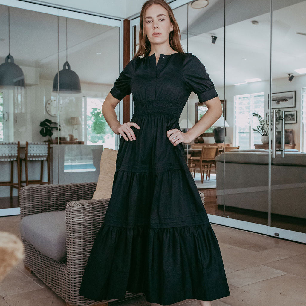 Woman in a black dress standing in a modern indoor setting with glass walls.