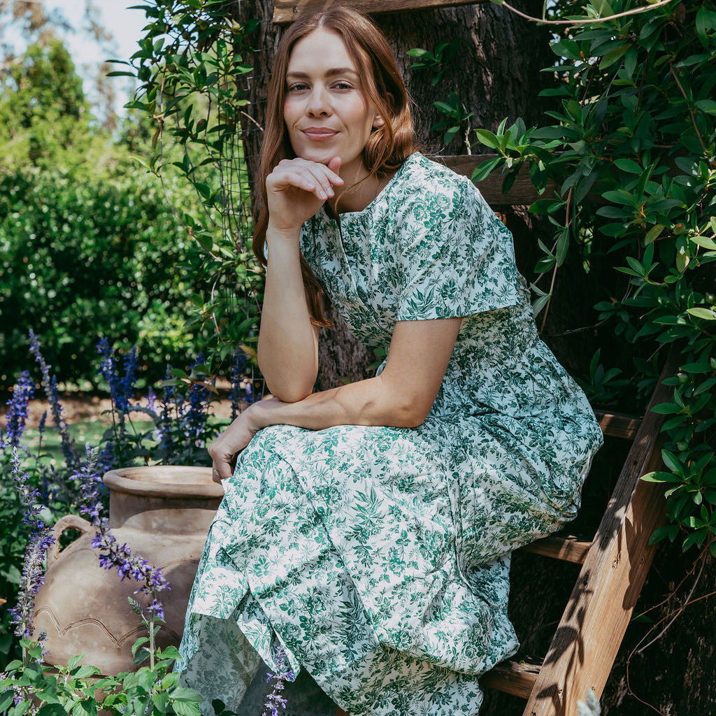 Woman in a floral dress sitting on a wooden ladder in a garden