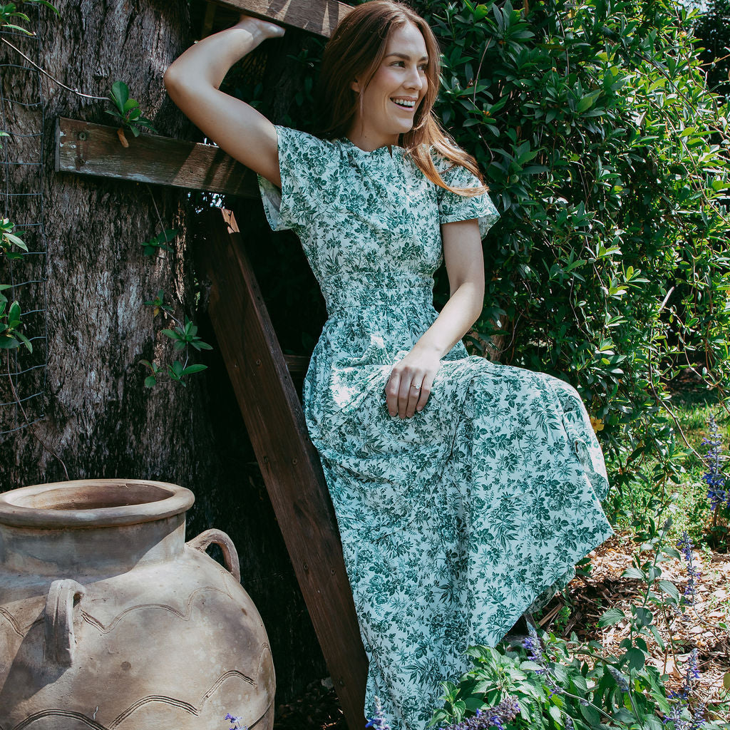 Woman in a floral dress sitting on a wooden ladder in a garden setting