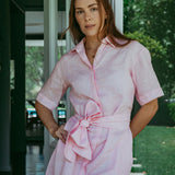 Woman wearing a pink dress with a belt standing outdoors.