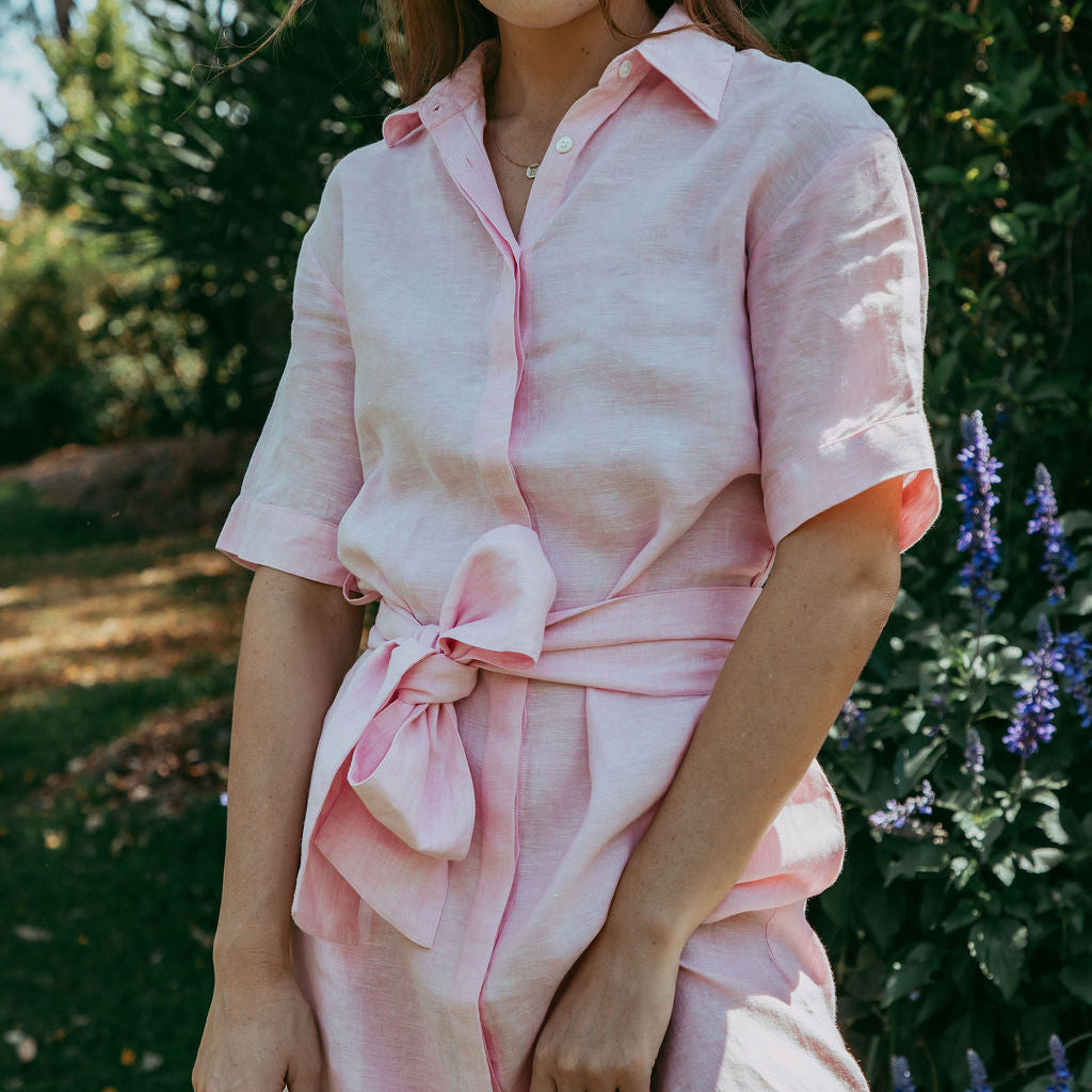 Woman wearing a pink outfit standing outdoors with greenery in the background