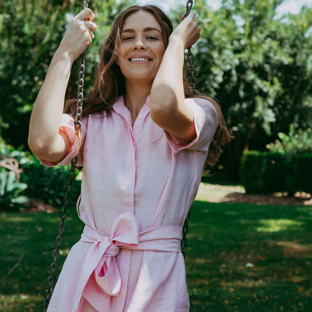 Woman in a pink dress swinging on a swing set with greenery in the background