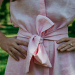 Close-up of a pink dress with a large bow detail, worn by a person outdoors.