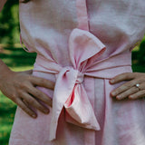 Close-up of a pink dress with a large bow detail, worn by a person outdoors.