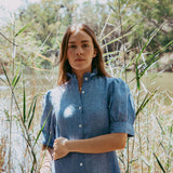Woman in a blue shirt standing in tall grass by a body of water