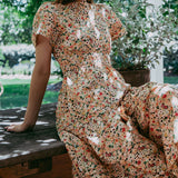 Woman in a floral dress sitting on a wooden bench outdoors with greenery in the background