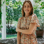 Woman in a floral dress standing outdoors with greenery in the background