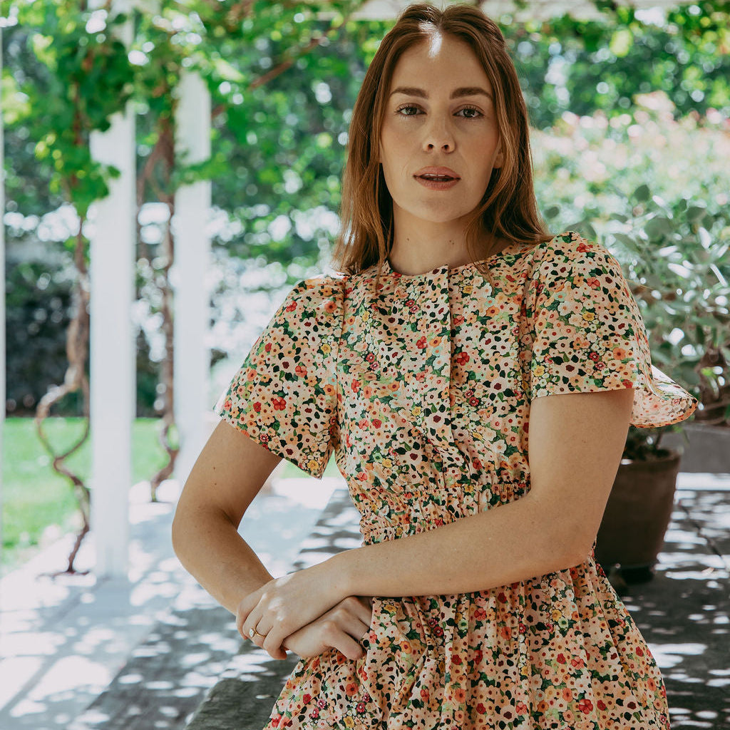 Woman in a floral dress standing outdoors with greenery in the background
