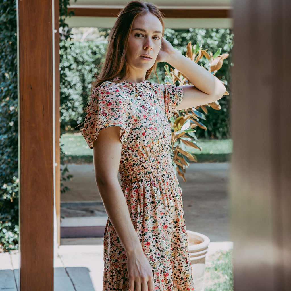 Woman in a floral dress standing outdoors near a house.