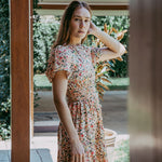 Woman in a floral dress standing outdoors near a house.