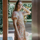 Woman in a floral dress standing outdoors near a house.