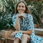 Woman in a blue floral dress sitting outdoors among plants