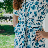 Person wearing a blue floral dress with a blurred outdoor background