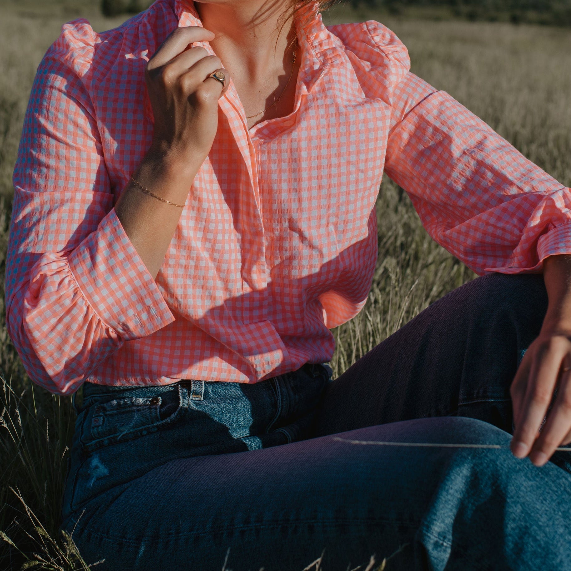 Person wearing a pink checkered shirt sitting in a field