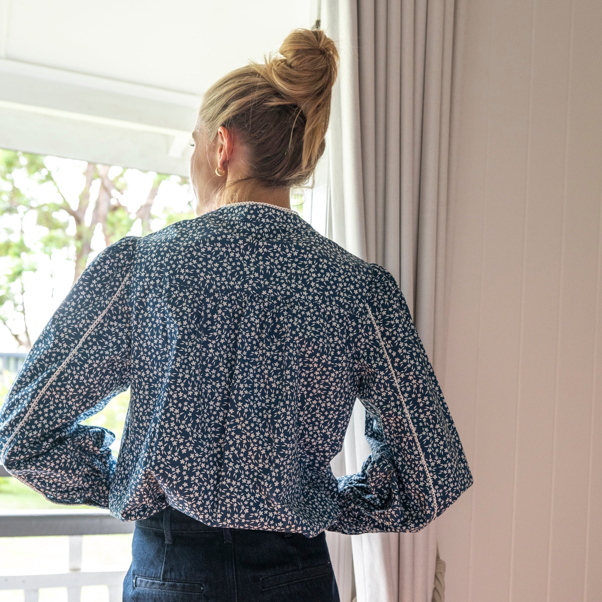 Rear view of navy floral blouse with white trim and covered buttons 