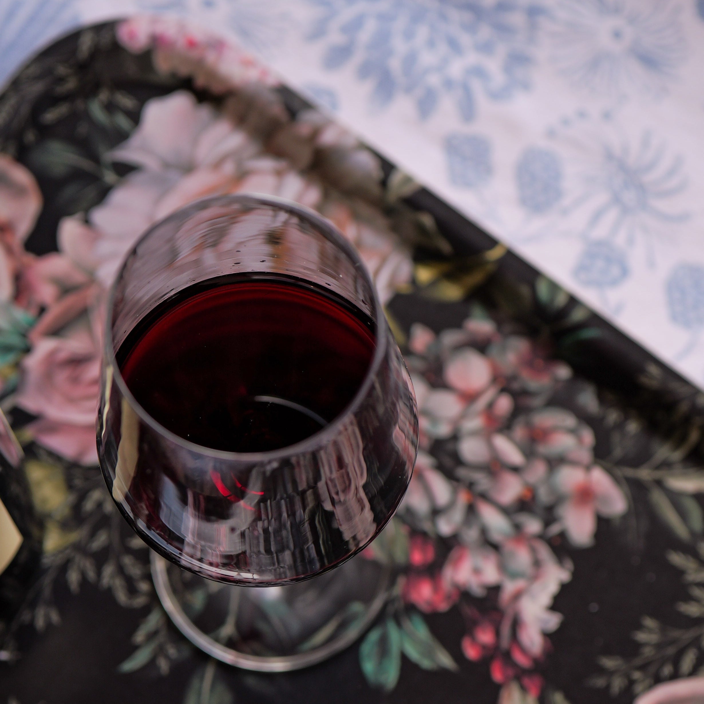 Glass of red wine on a floral-patterned tray with a white napkin.