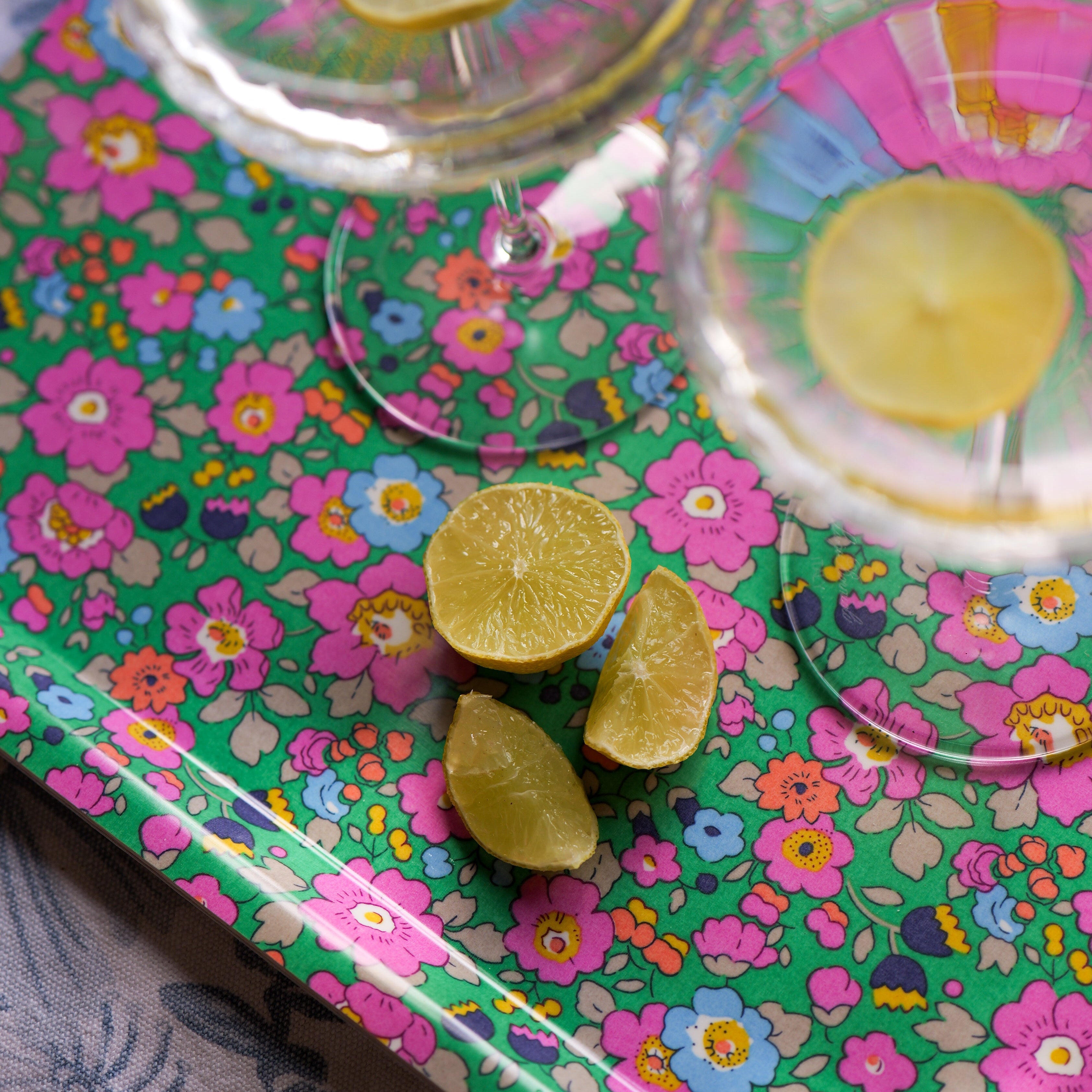 Lime slices on a colorful floral-patterned tray with a glass of yellow liquid.