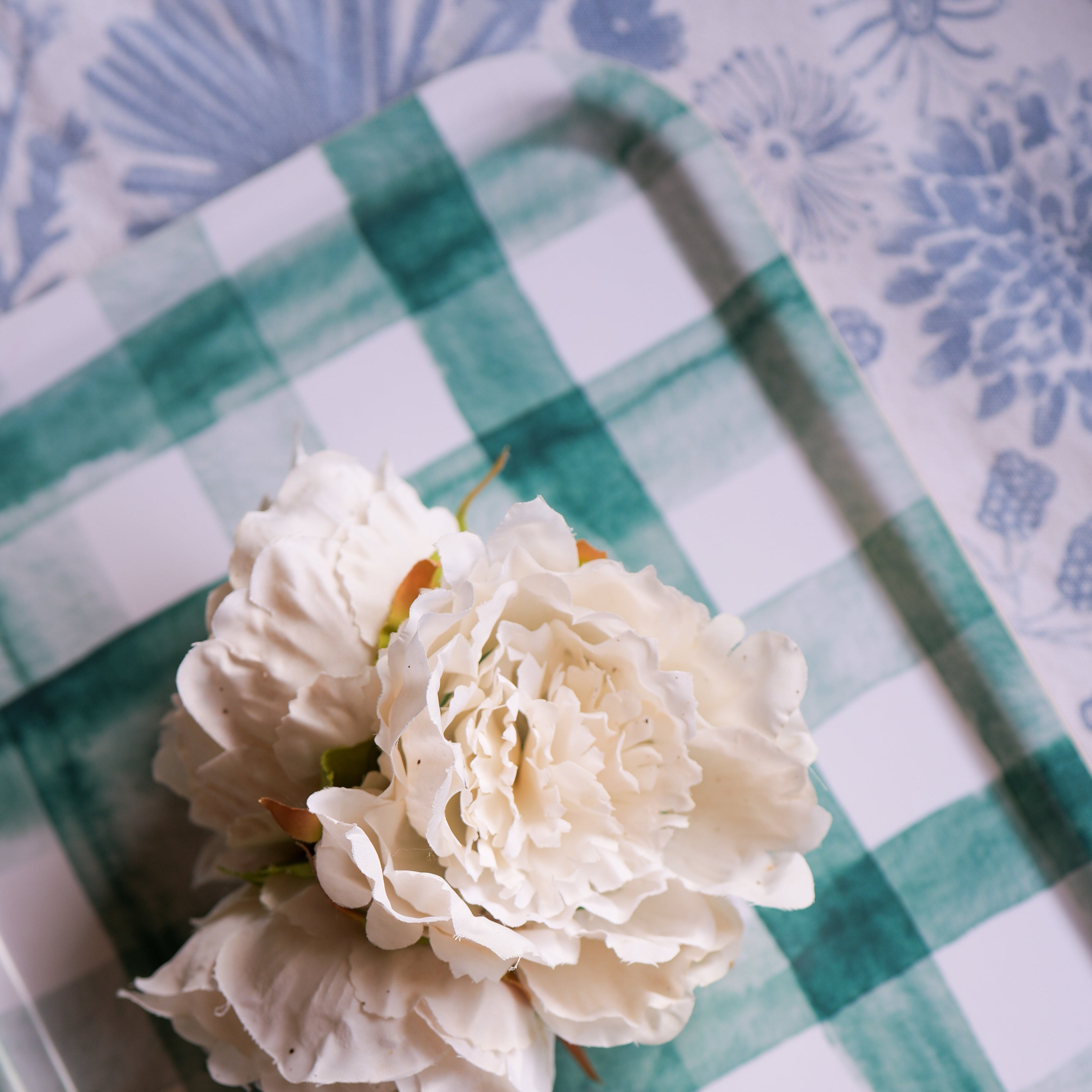 White flower on a green and white checkered tray with a floral-patterned background