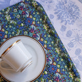 Ceramic cup and saucer on a floral placemat with a white floral tablecloth background