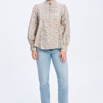 Woman wearing a patterned blouse and light blue jeans on a white background