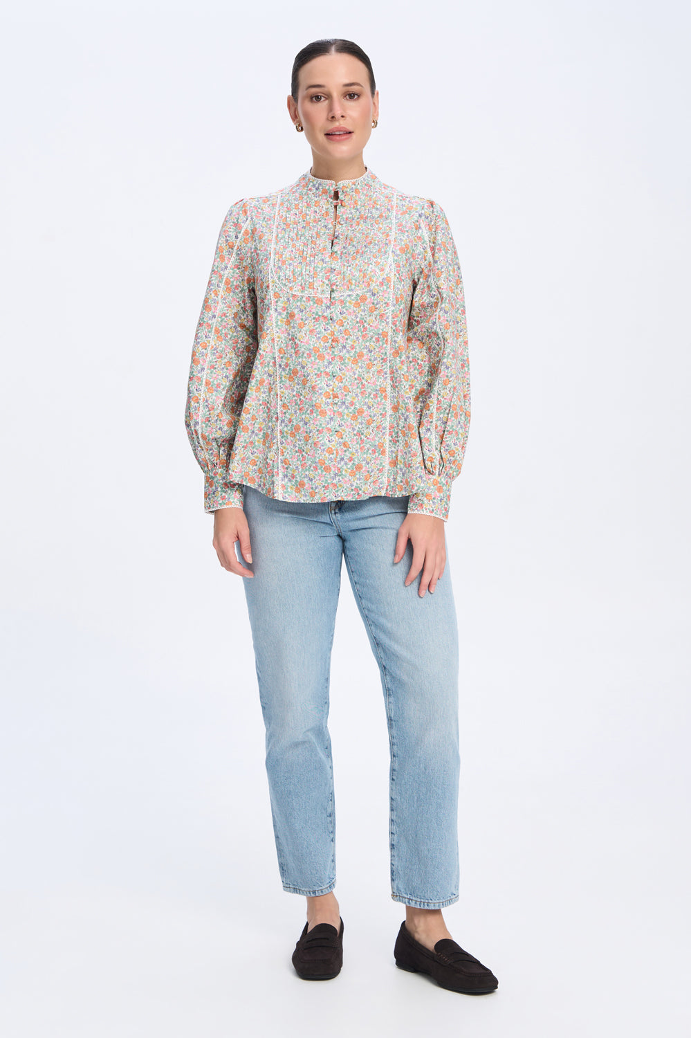 Woman wearing a patterned blouse and light blue jeans on a white background